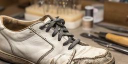 Sneaker in pelle segnata dall'uso prima della riparazione artigianale